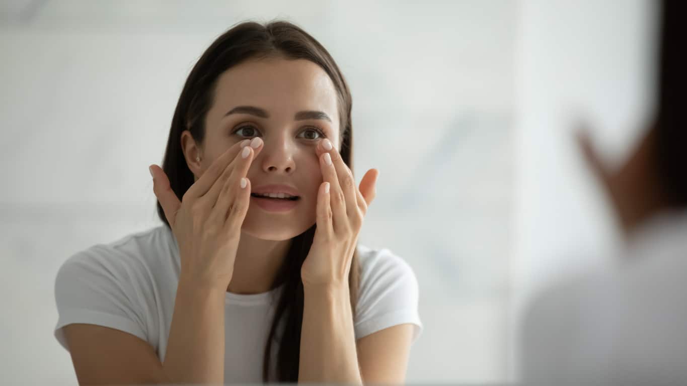 Woman looking in the mirror at her skin after microneedling in Plano, TX