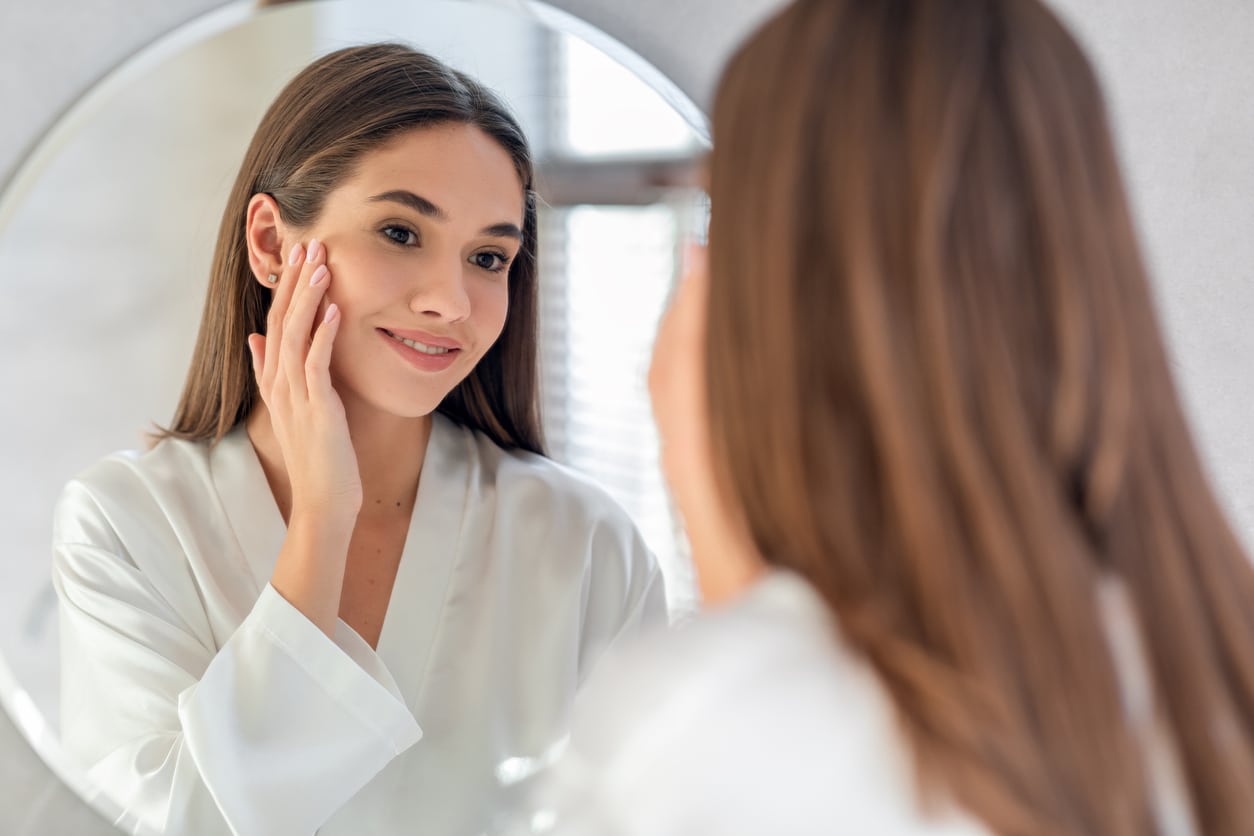 Woman looking in the mirror after skincare routine from skin analysis in Plano, TX